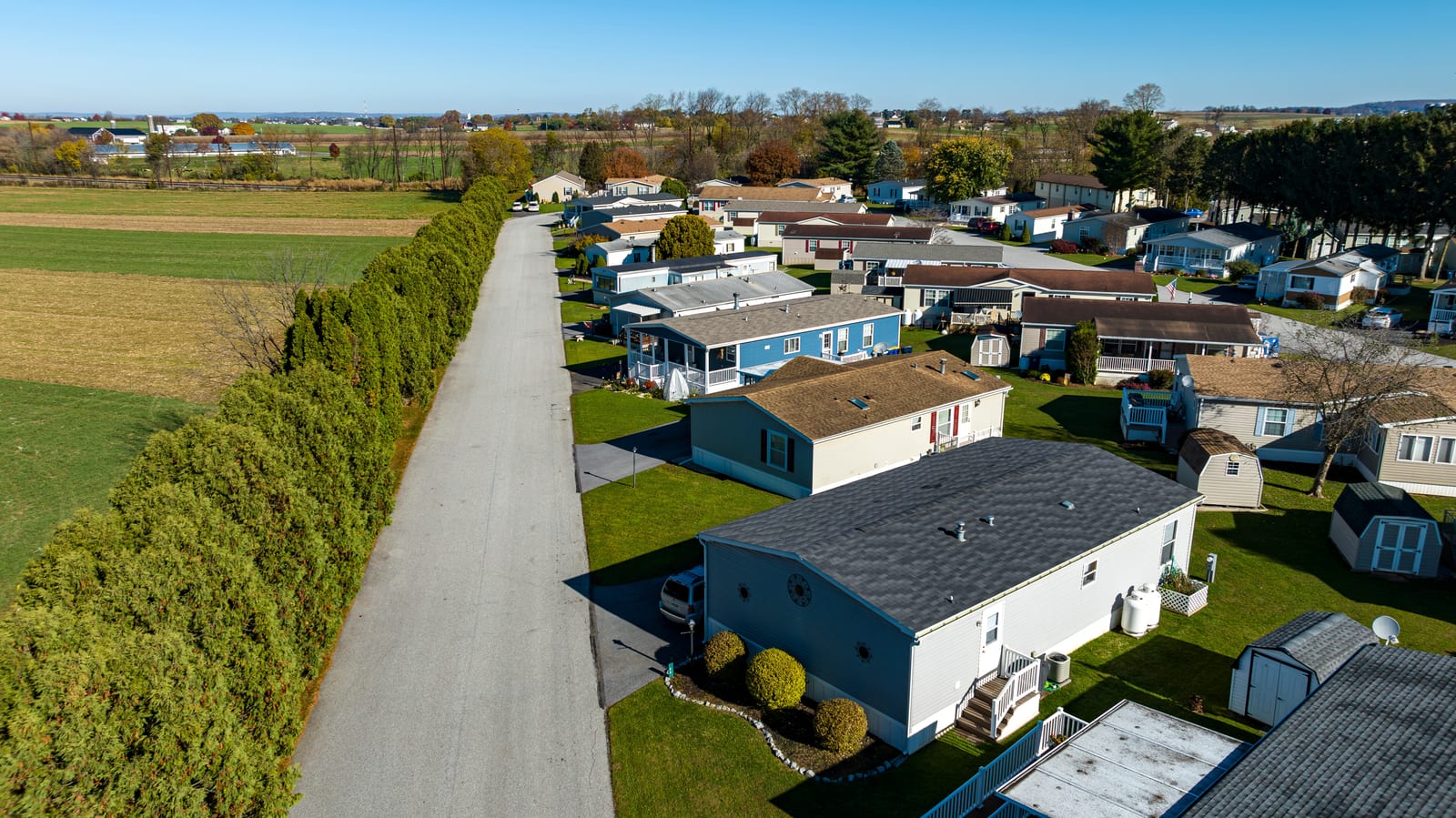 A manufactured home community seen from above, showing its access road, home sites and surrounding open land