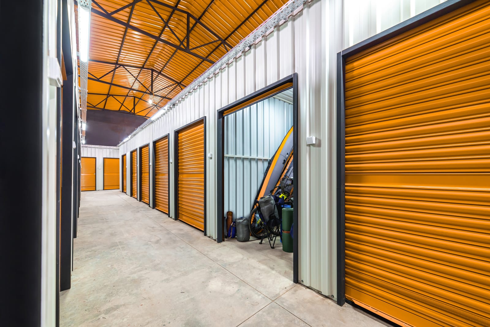 Interior corridor of a self-storage building lined with roll-up unit doors, one standing open